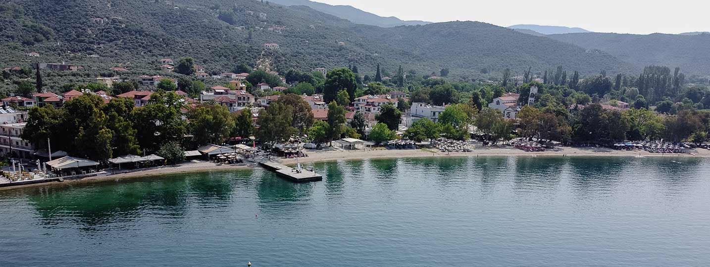 Aerial view of a peaceful coastal village in Pelion, Greece, with a beach, pier, and surrounding hills – perfect vacation spot