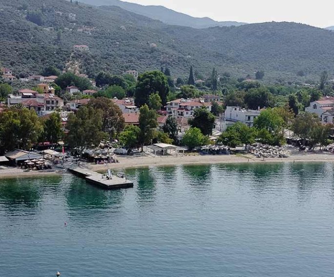 Aerial view of a peaceful coastal village in Pelion, Greece, with a beach, pier, and surrounding hills – perfect vacation spot