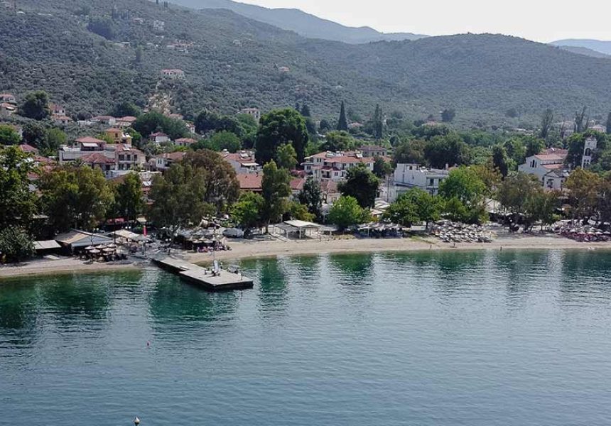 Aerial view of a peaceful coastal village in Pelion, Greece, with a beach, pier, and surrounding hills – perfect vacation spot