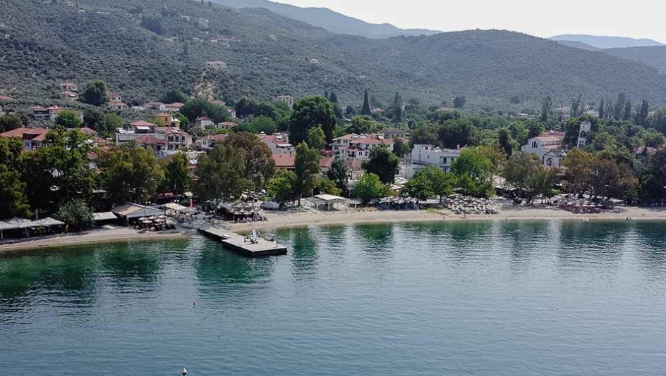 Aerial view of a peaceful coastal village in Pelion, Greece, with a beach, pier, and surrounding hills – perfect vacation spot