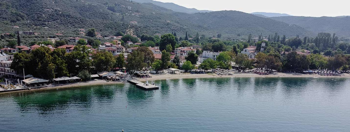 aerial-pelion-seaside-town Aerial view of a peaceful coastal village in Pelion, Greece, with a beach, pier, and surrounding hills – perfect vacation spot