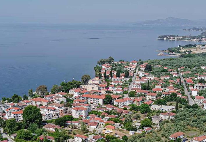 pelion-coastal-village-view-pelion-villas Aerial view of a coastal village in Pelion with red-roof houses, olive trees, and the calm sea of Pagasetic Gulf in the background.