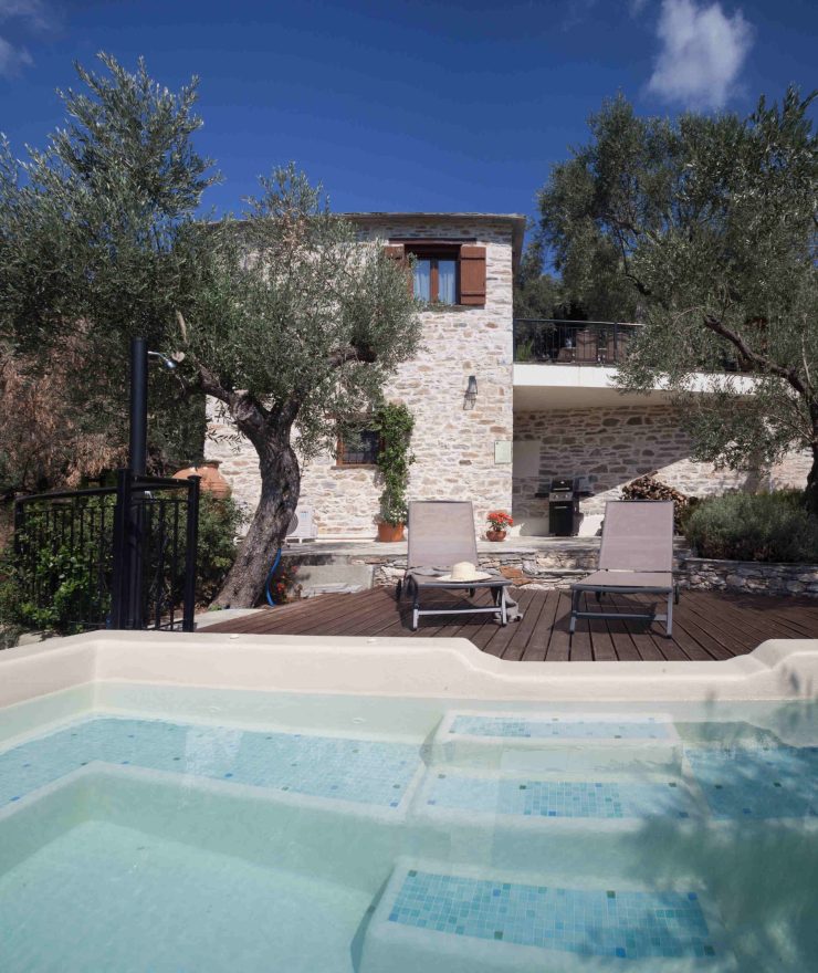 Μια ήρεμη πισίνα με ξαπλώστρες μπροστά από τη λιθόκτιστη Villa Ioanna, περιτριγυρισμένη από ελαιόδεντρα, στο Pelion-villas.com.