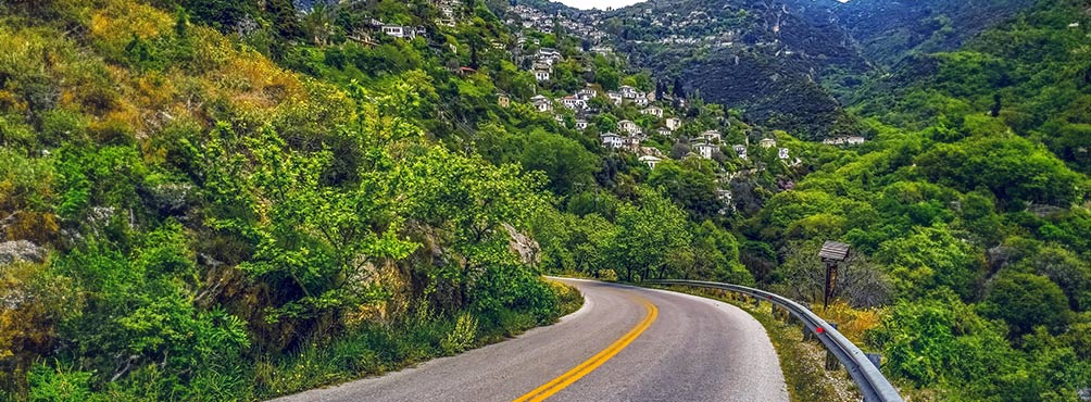 Ορεινός δρόμος με καταπράσινη φύση και παραδοσιακά σπίτια σε πλαγιά