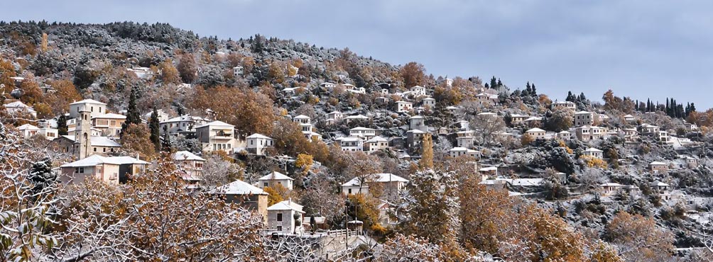 Ορεινό χωριό στο Πήλιο με χιονισμένες στέγες και φθινοπωρινά δέντρα