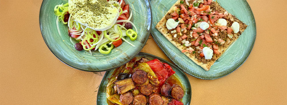 Λήψη από πάνω με τρία παραδοσιακά ελληνικά πιάτα: χωριάτικη σαλάτα με φέτα, πίτα με κιμά και ντομάτα, και σπετσοφάι με λουκάνικο και πιπεριές.