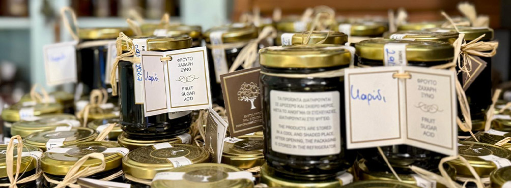 A collection of handmade Greek walnut spoon sweets in labeled jars, traditionally preserved and sold in Pelion.