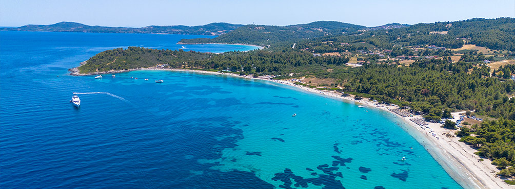Αεροφωτογραφία μεγάλου τιρκουάζ κόλπου με παραλία και πευκόφυτους λόφους στη Σιθωνία Χαλκιδικής.