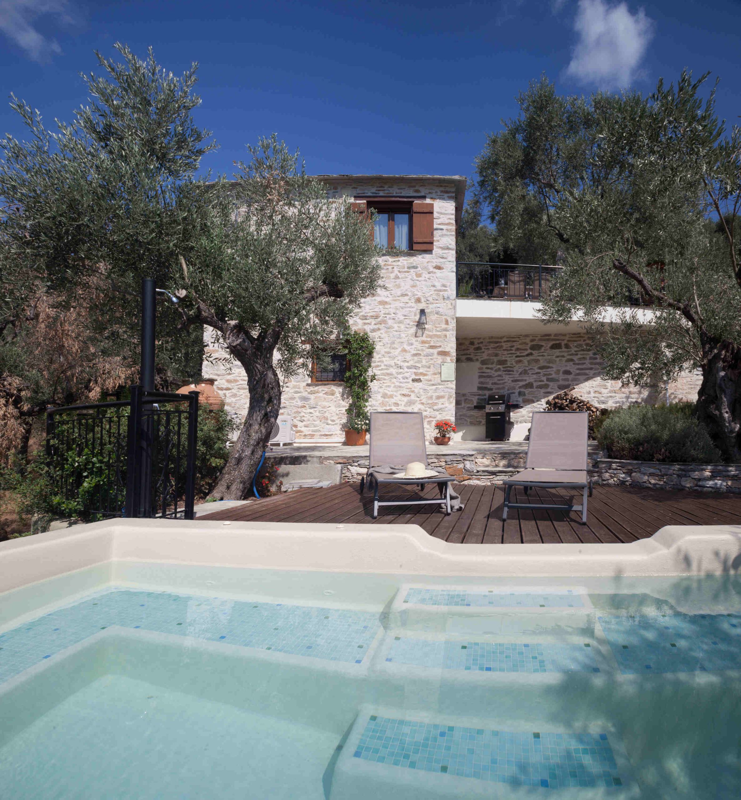 A serene pool with sunbeds overlooking the stone-built Villa Ioanna surrounded by olive trees, at Pelion-villas.com.