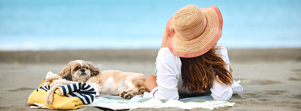Woman in a straw hat lying on the beach with a small dog on a towel